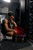 Man in a gym setting opening a red and black bag.