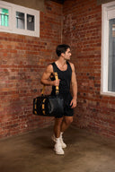 Man in black gym attire wearing a black leather gym bag with a shoulder strap