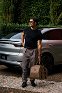 Man in black shirt and gray pants holding a beige bag, standing next to a silver car.