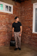 Man standing in a room with brick walls holding a black leather gym bag.