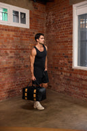 Male in black gym attire holding black leather gym bag in hand against a red brick wall