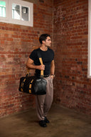 Man holding a black duffel bag against a brick wall