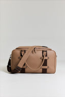 Photo of brown leather gym bag against white background with shoulder strap draped over the top