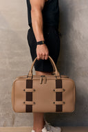 Person holding a tan leather bag with brown accents against a neutral background